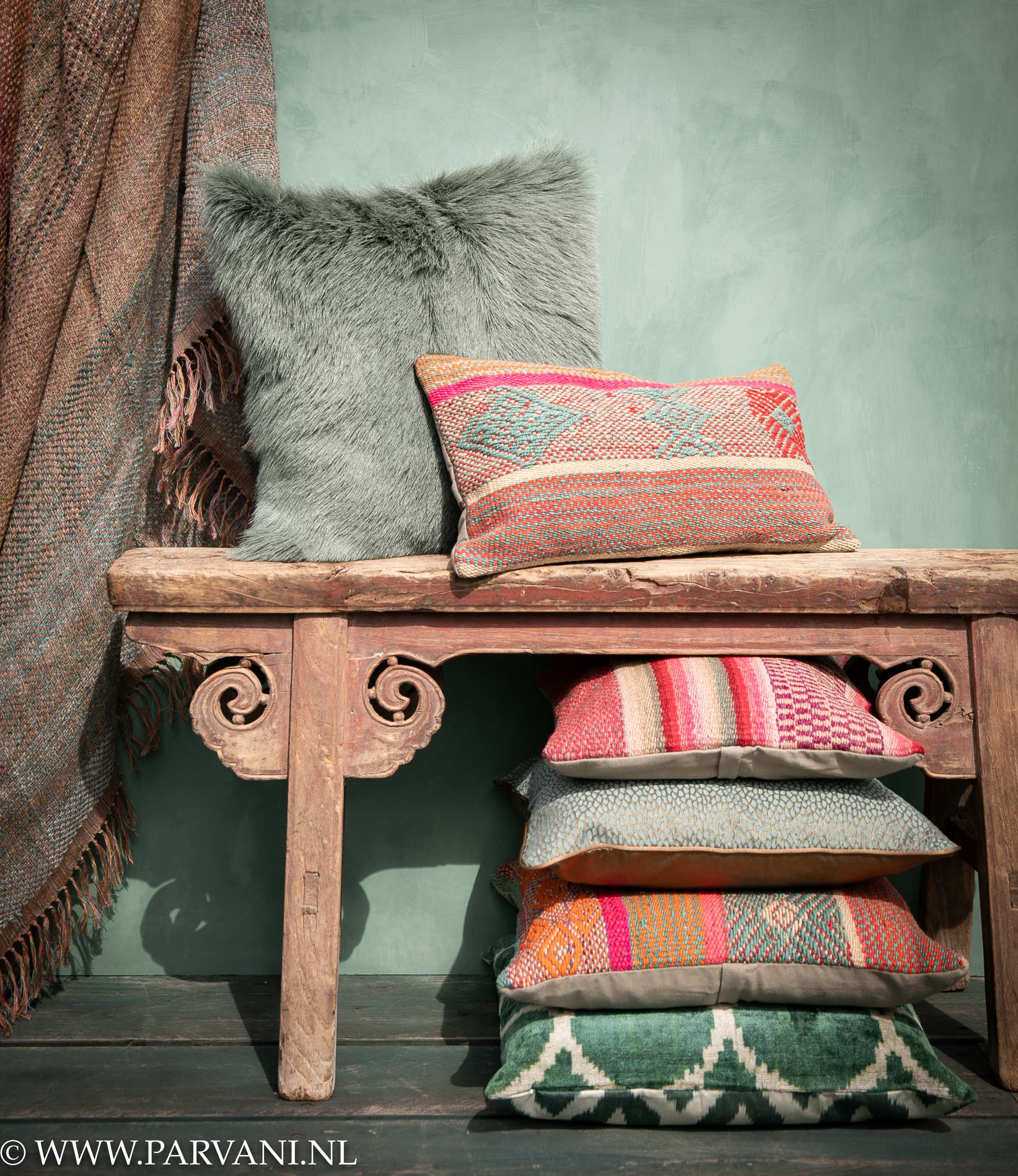 Kleurrijke sierkussens en plaid met roze groen turquoise rood oranje kleuren op oud houten bankje