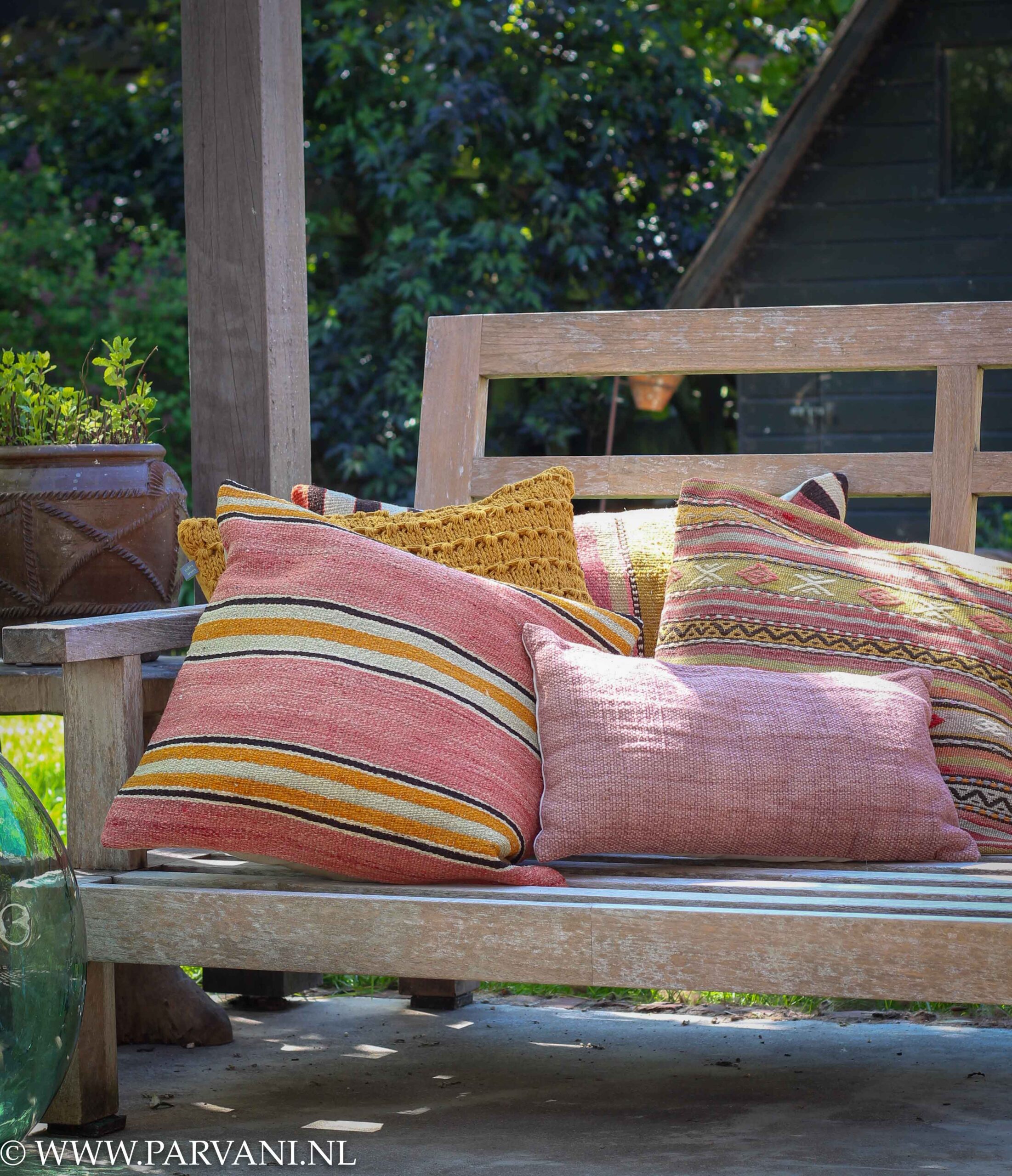 Kelim kussens op tuinbank in warme kleuren oud roze en geel