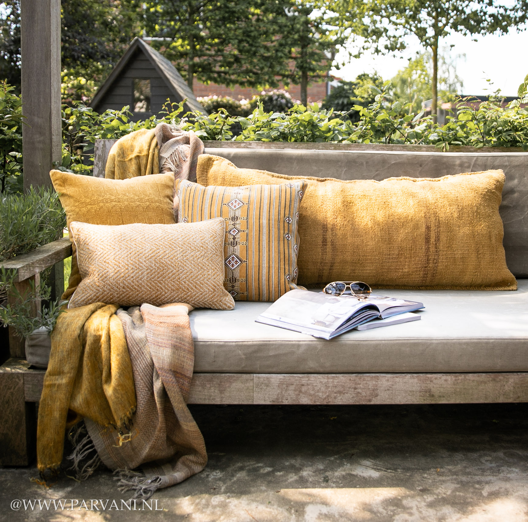 gele kussens en plaids op buitenbank grote rugkussens