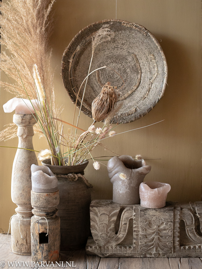 Woonaccessoires in warme naturel kleuren met Indiase kandelaars met snijwerk, kaarsen en oude houten pot