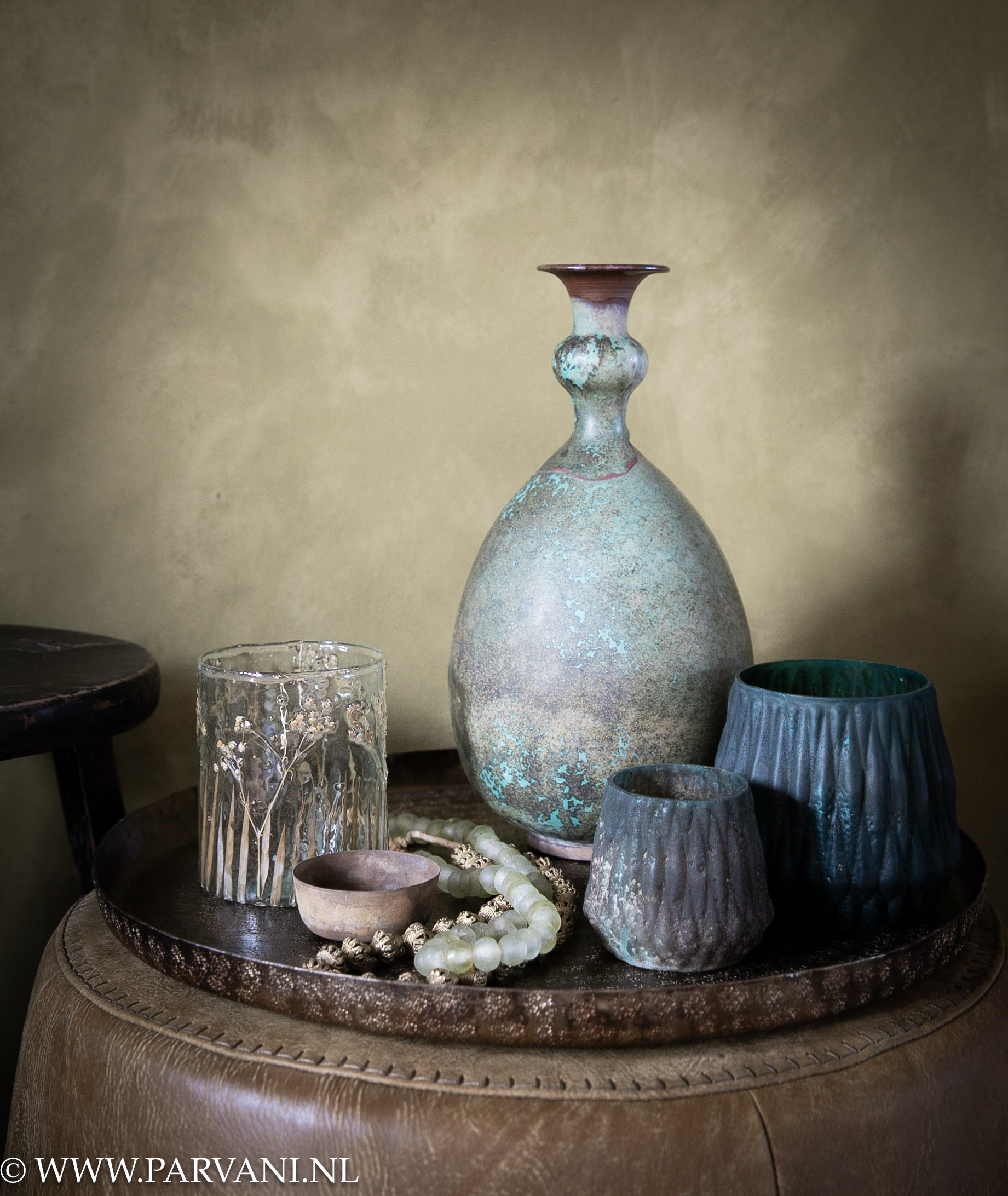 Brass dienblad met Chinese aardewerk vaas, wax glazen en kettingen op groene ronde lederen poef