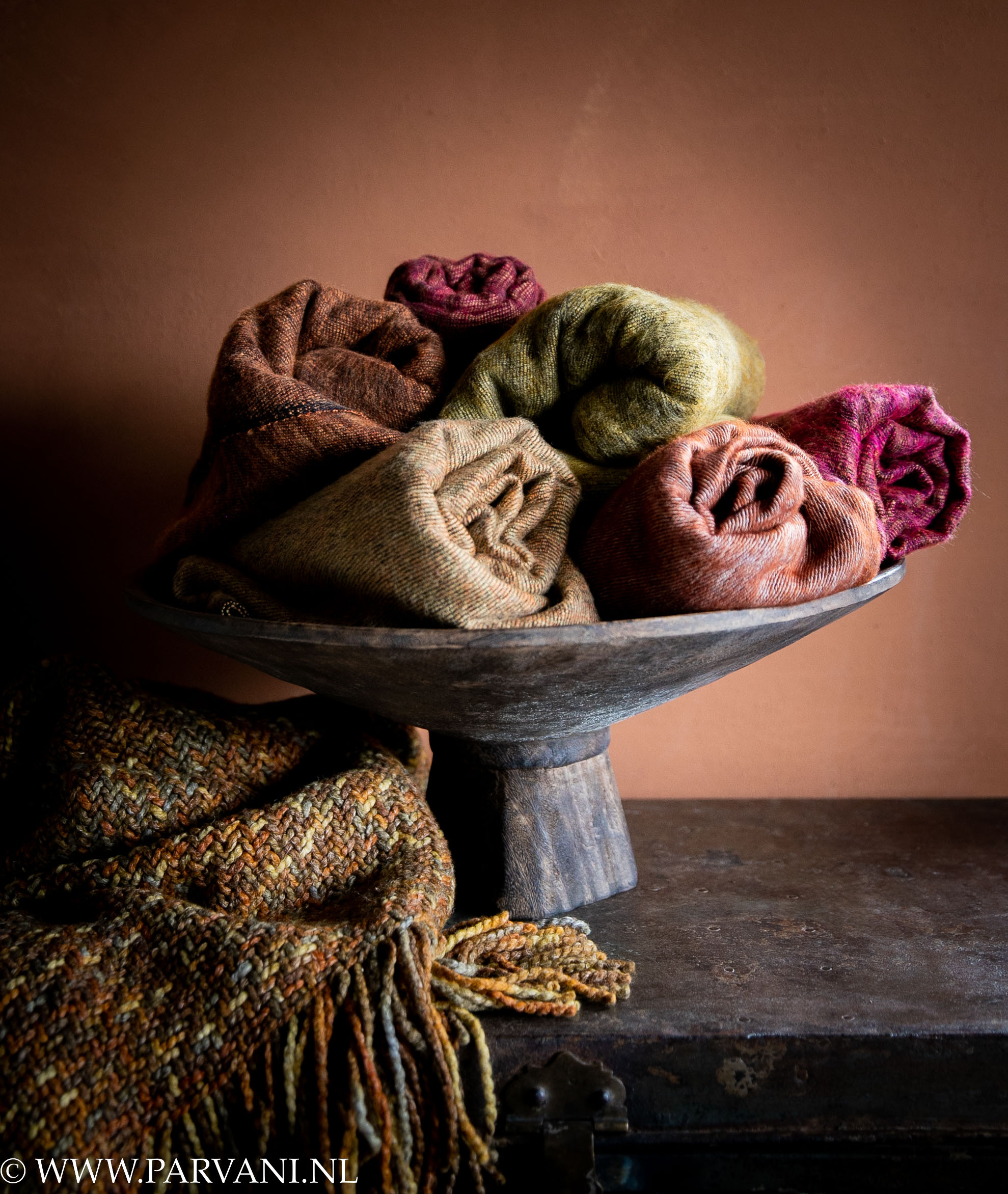 Yakwollen sjaals uit Nepal met omslagdoek poncho van Manos del Uruguay in warme kleuren oranje, terra, oker en roze op een houten fruitschaal uit Indonesië