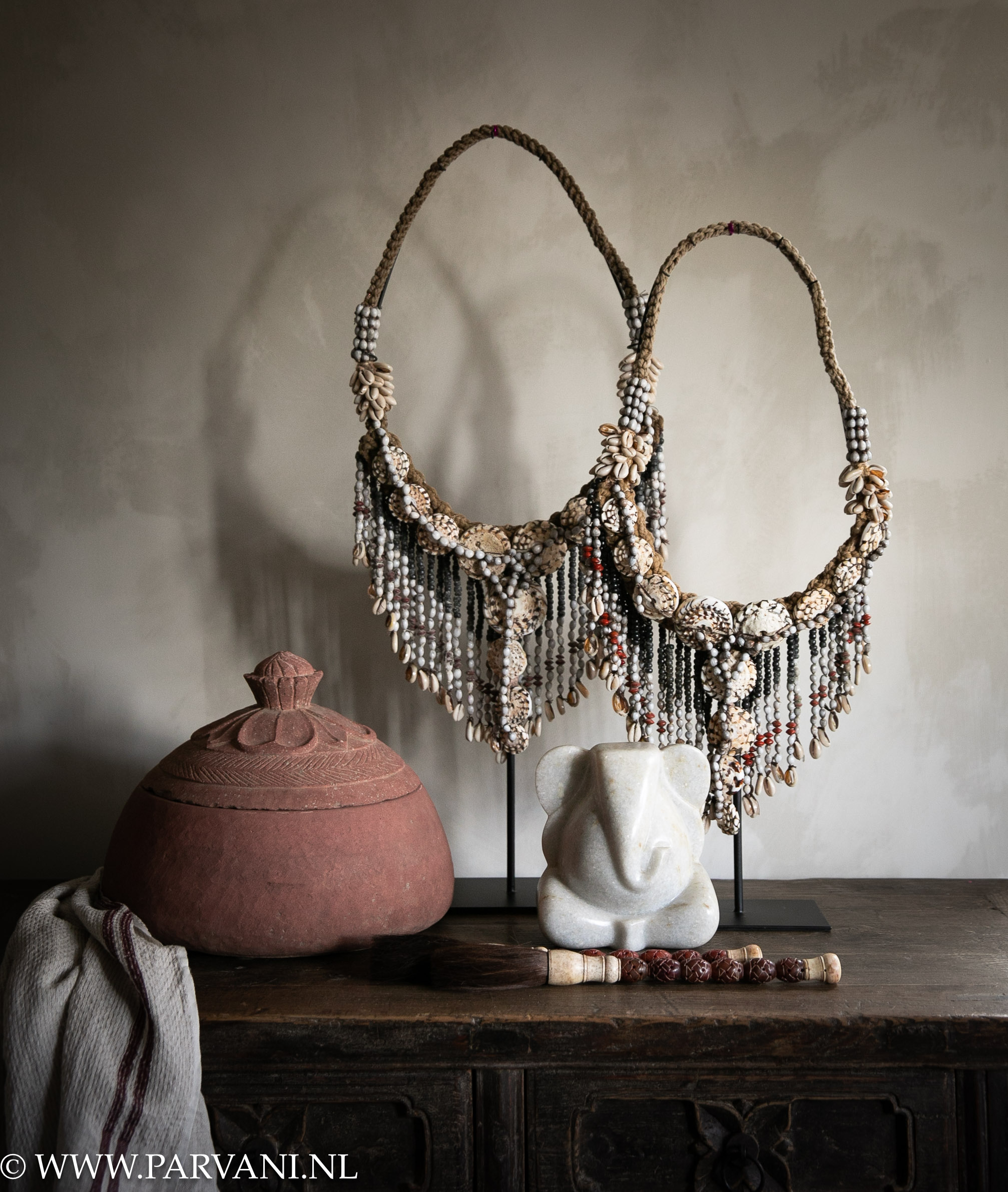 Decoratieve schelpen kettingen op standaard met wit marmer Ganseha beeldje en grote terracotta pot met deksel en roodbruine kalligrafiekwasten
