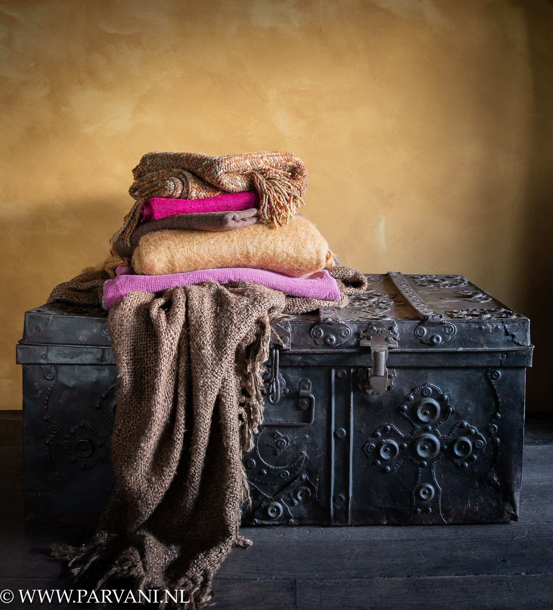 Grote vintage ijzeren koffer met veel mooie details uit India met stapel kleurrijke plaids en sjaals in oker, bruin en roze kleuren