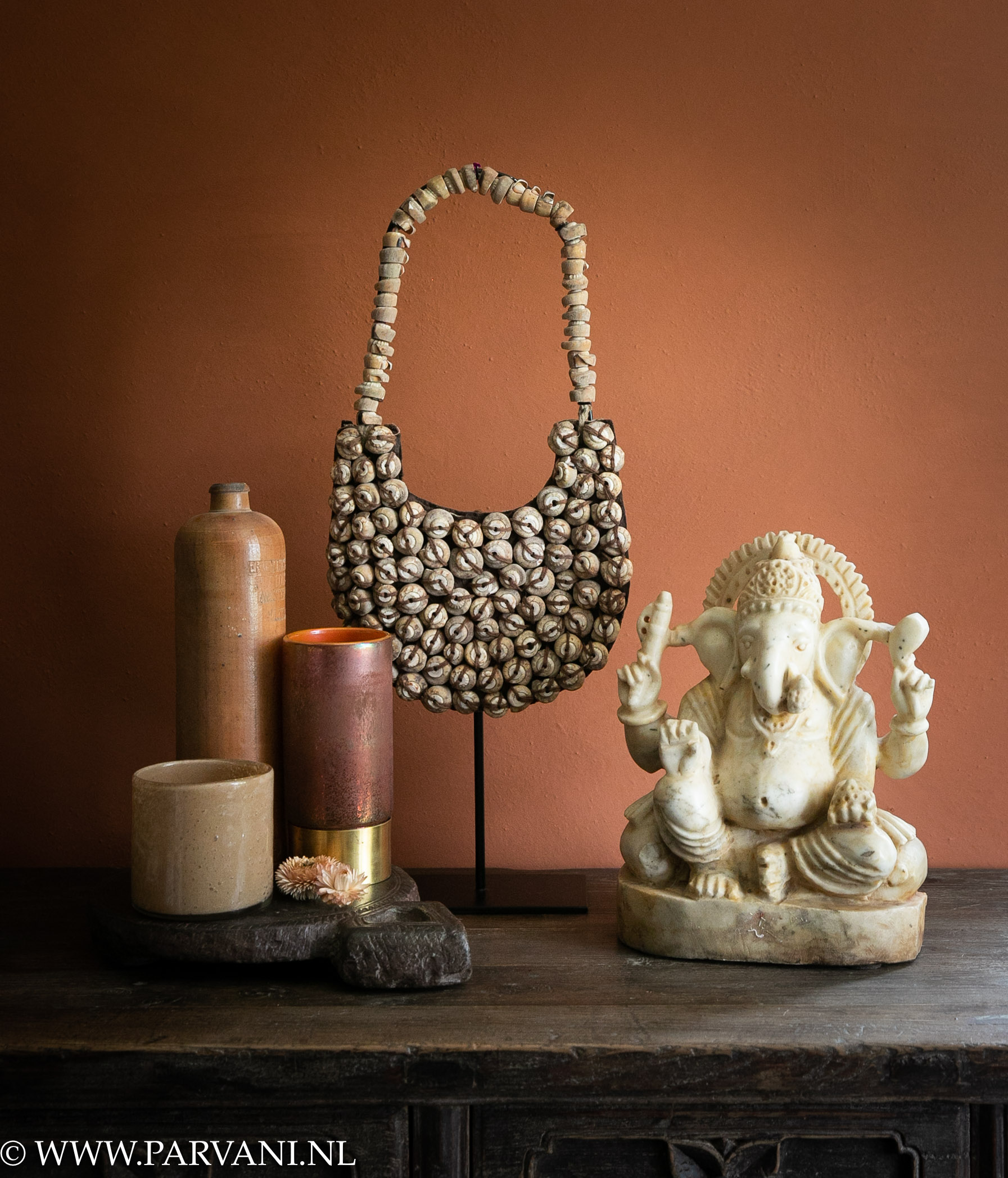 Indiaas Ganesh beeld marmer met schelpenketting op standaard en oude aardewerk kruik met wax glazen in warme oranje tinten