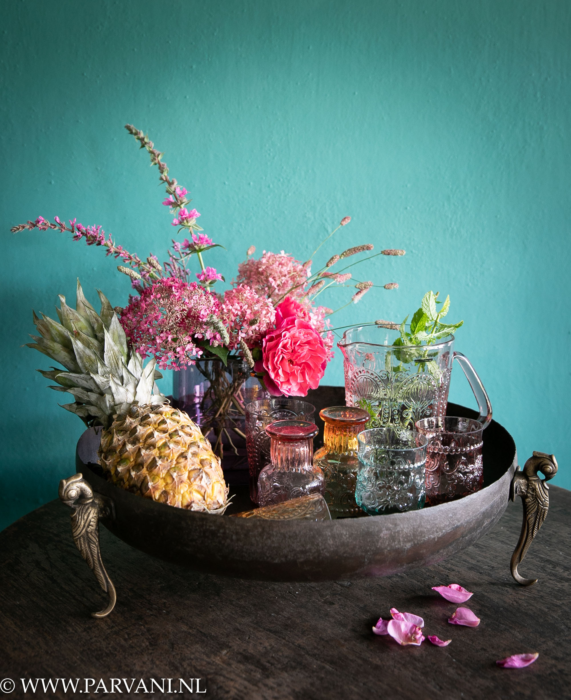 Ronde bruin ijzeren schaal, tray uit India met messing peacock pootjes, gekleurd glaswerk in roze oranje en blauwgroen met waterkan en roze vaas met verse bloemen