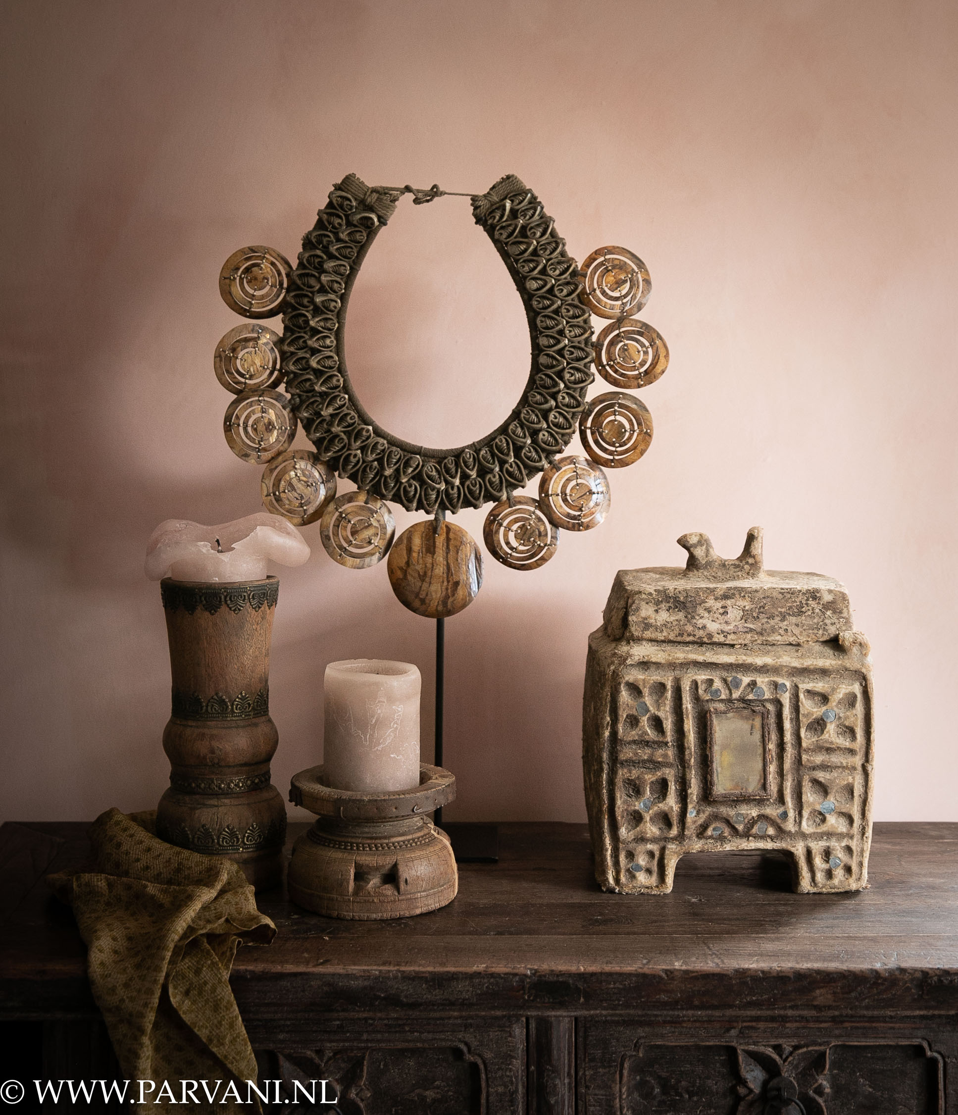 Woonaccessoires in bruine tinten met Indiaas kistje van papier maché met houten kandelaars en grote schelpenketting op standaard