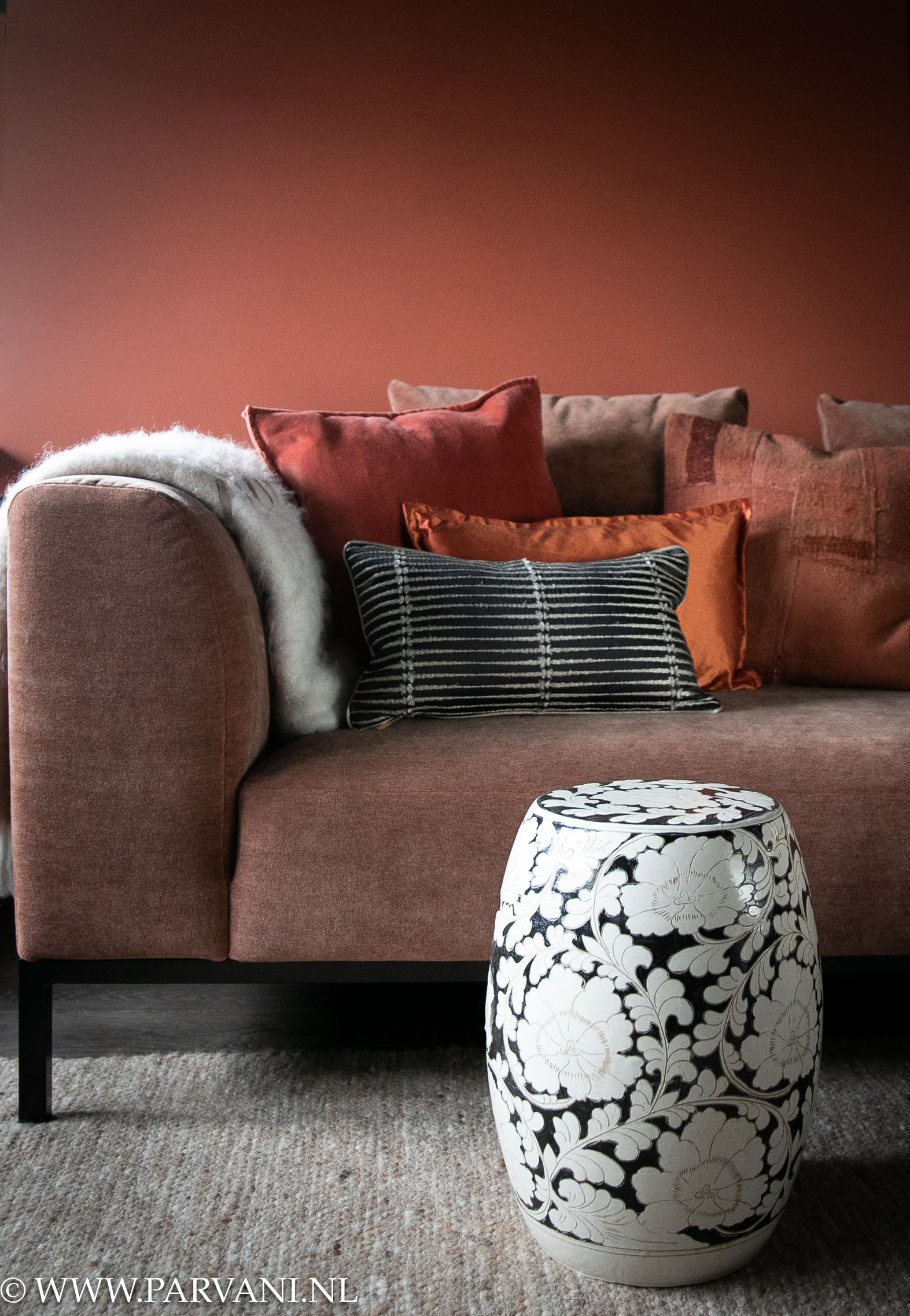 Ronde bijzettafel in zwart wit aardewerk met mooi patroon bij terra roze bank met kussens en plaid in warme oranje kleuren