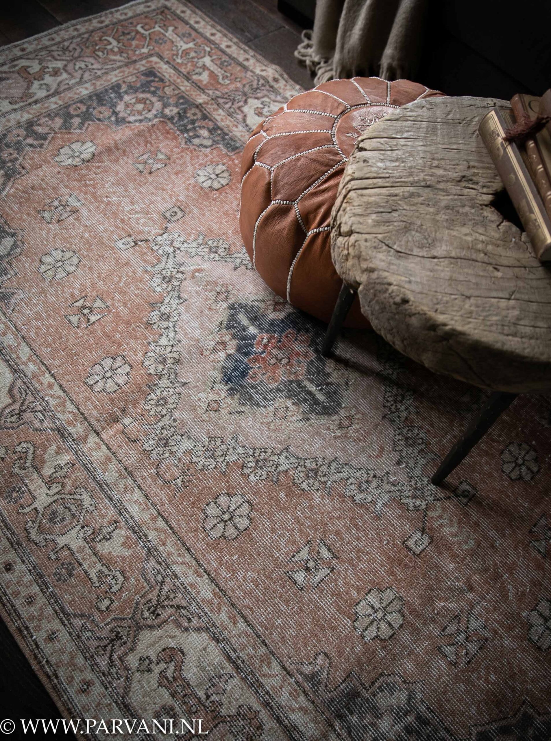 Vintage tapijt met mooi patroon in warme roze terra kleuren met donkerblauwe accenten en bruin cognac leren poef