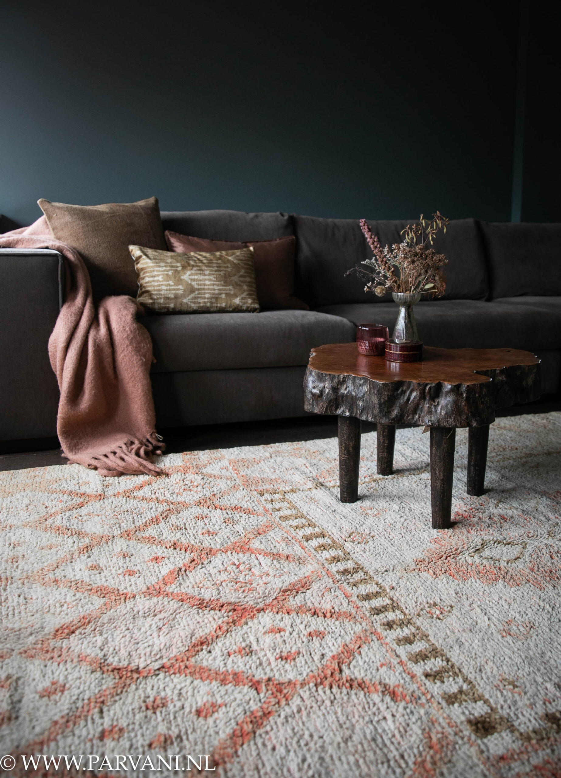 Wollen berber tapijt in lichte beige basiskleur met patroon in warme terra oranje en bruintinten met houten boomstam tafeltje