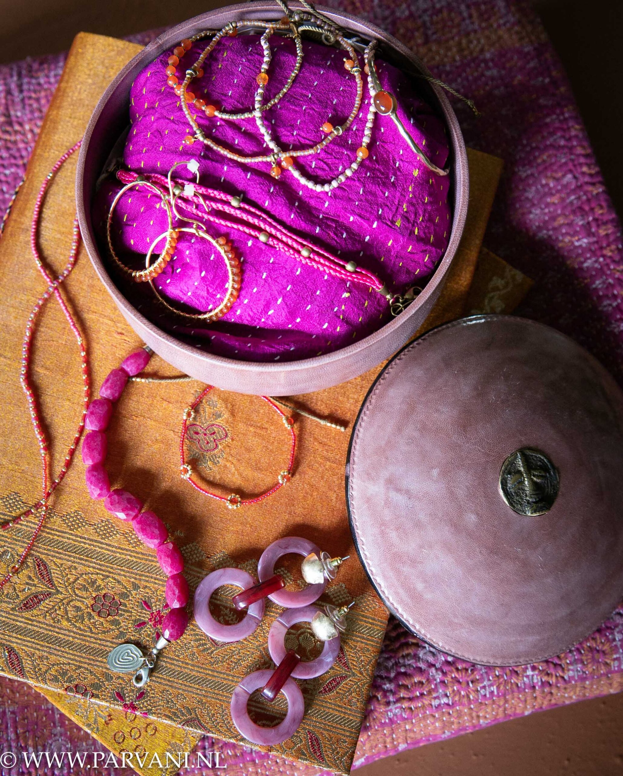 Fairtrade sieraden, armbandjes, oorbellen en ketting in warme oranje roze kleuren met sari notebooks, plaid en rond leren doosje
