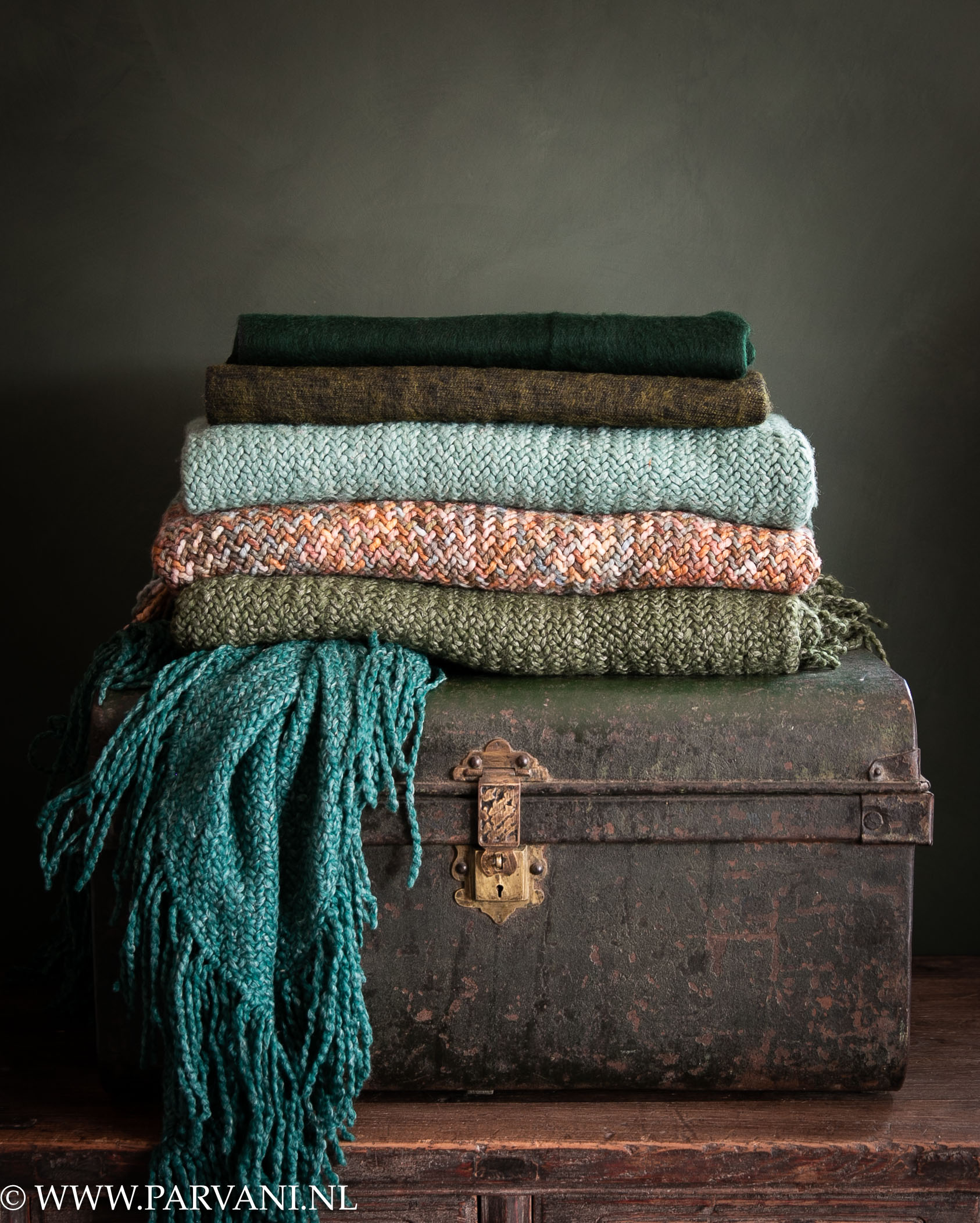 Kleurrijke poncho's omslagdoeken van Manos del Uruguay en yakwollen sjaals op oude groene metalen koffer uit India