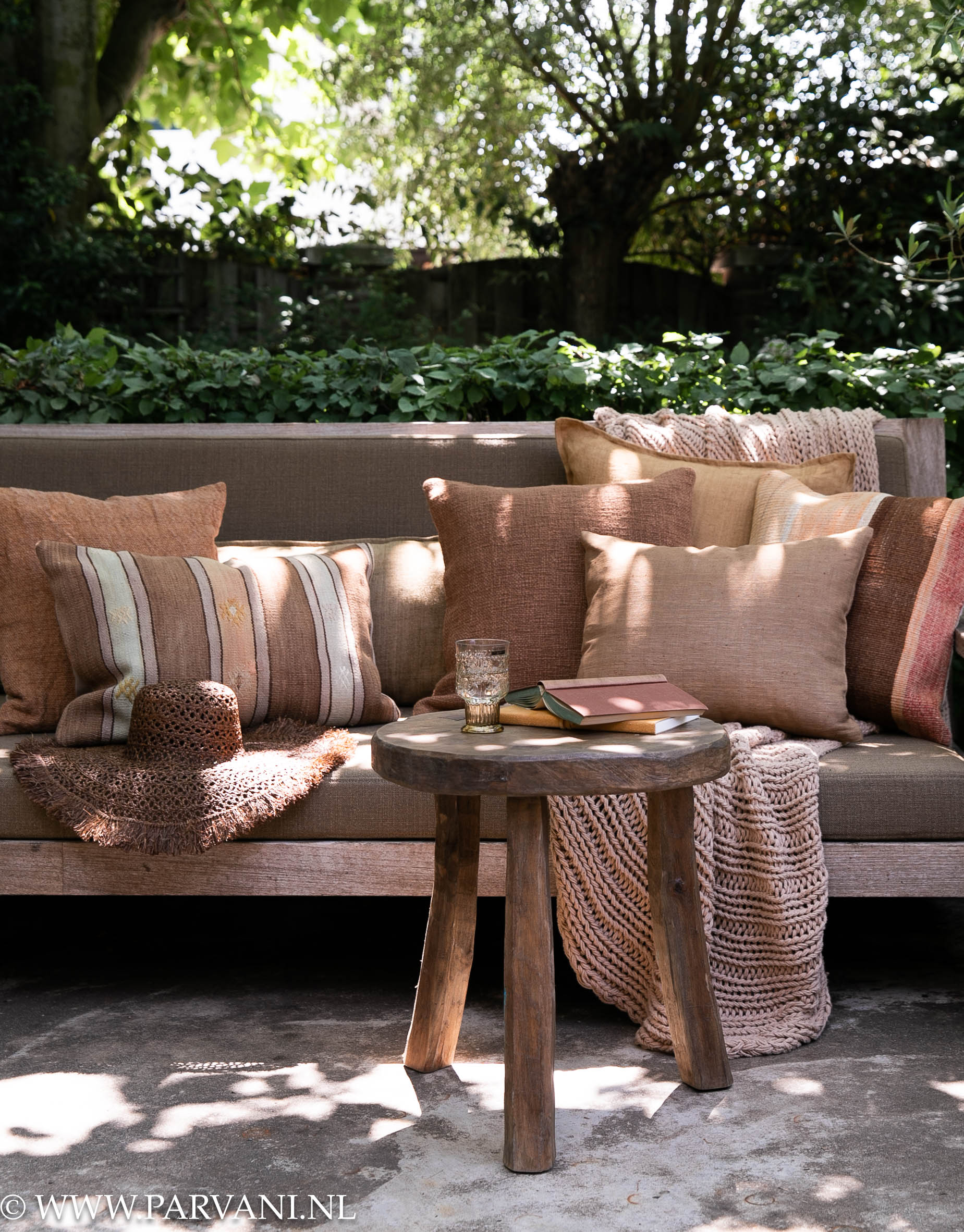 Kussens en plaid op tuinbank met kelim in warme bruin, camel en oud roze terra kleuren met rond houten bijzettafeltje