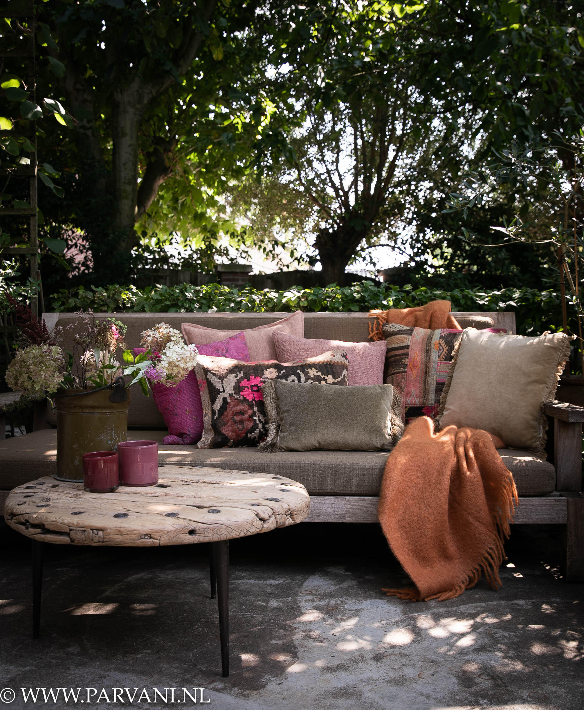 Loungebank met mix van kleurrijke kussens en wollen plaid in roze paars groen en oranje tinten met kelim, patroon en zachte velvet en linnen