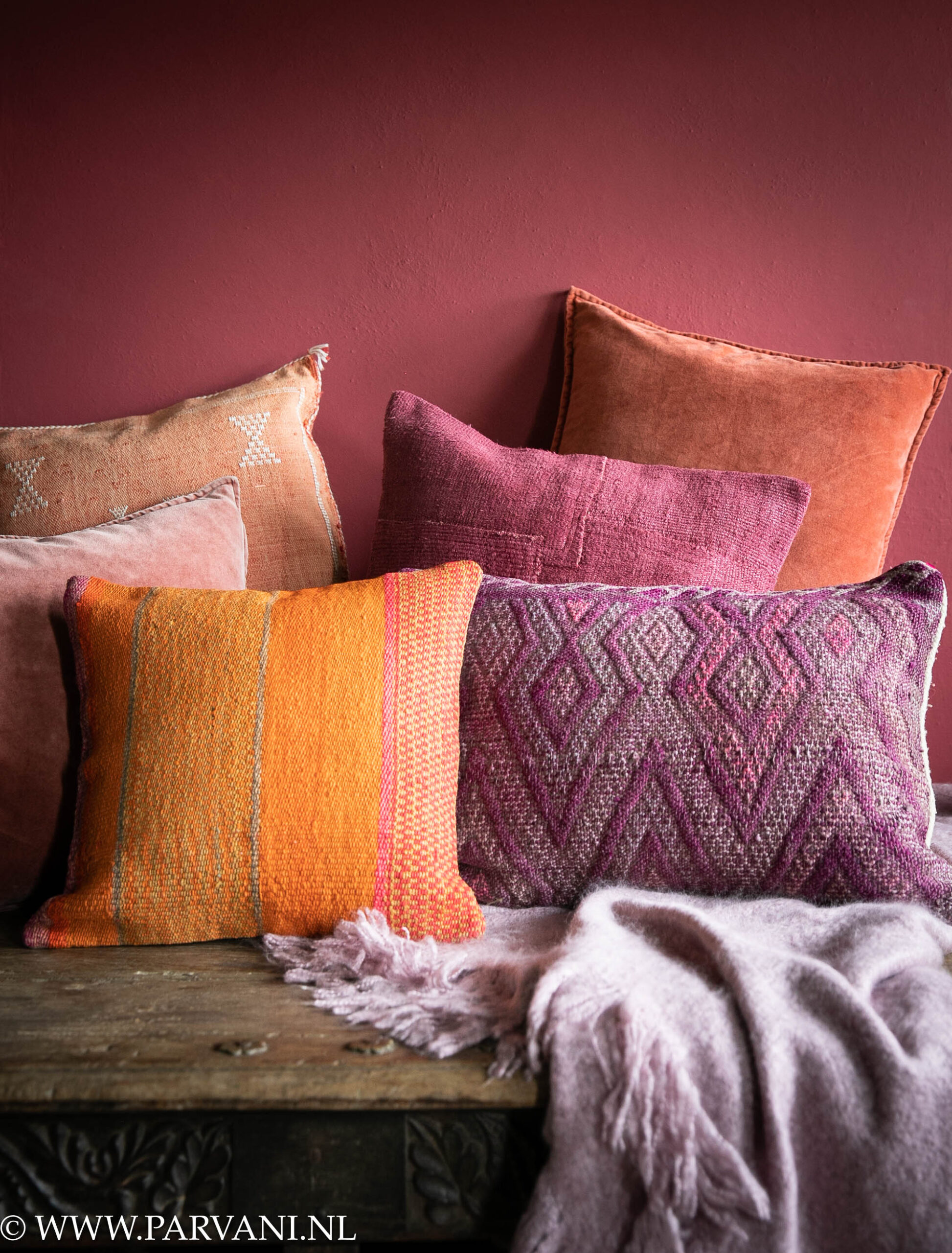 Mix kleurrijke kussens en plaid in warme cyclaam, roze, oranje, en paarse tinten met Boliviaans, kelim, velvet en hennep