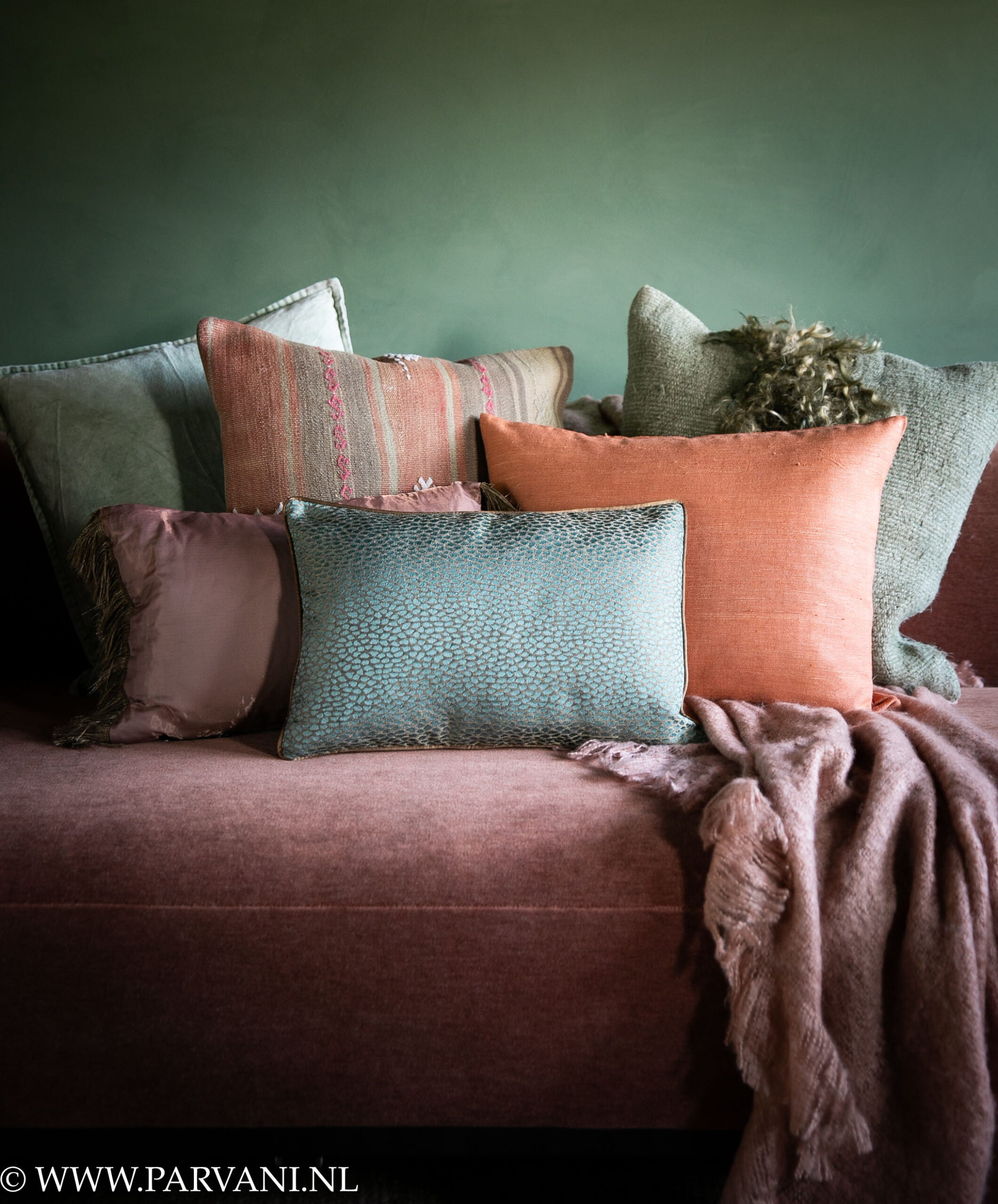 Mix kussens en plaid in warme kleuren oranje, roze, turquoise en zacht groene kleuren met kelim, vacht, velvet en patroon op terra oranje bank