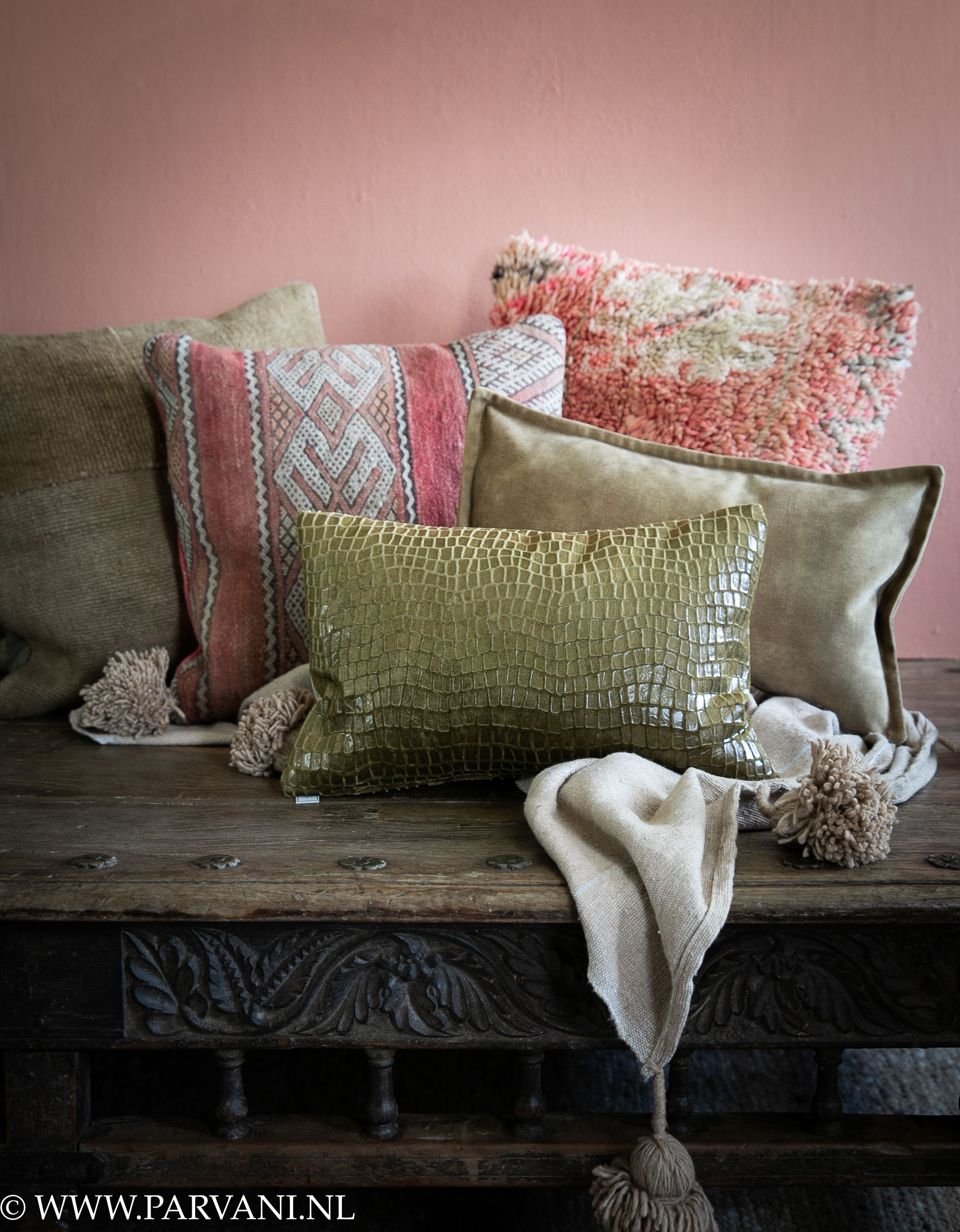 Mix van kussens in warme kleuren roze oranje en geelgroen met velvet, hennep en kelim uit Marokko op oude Indiase salontafel