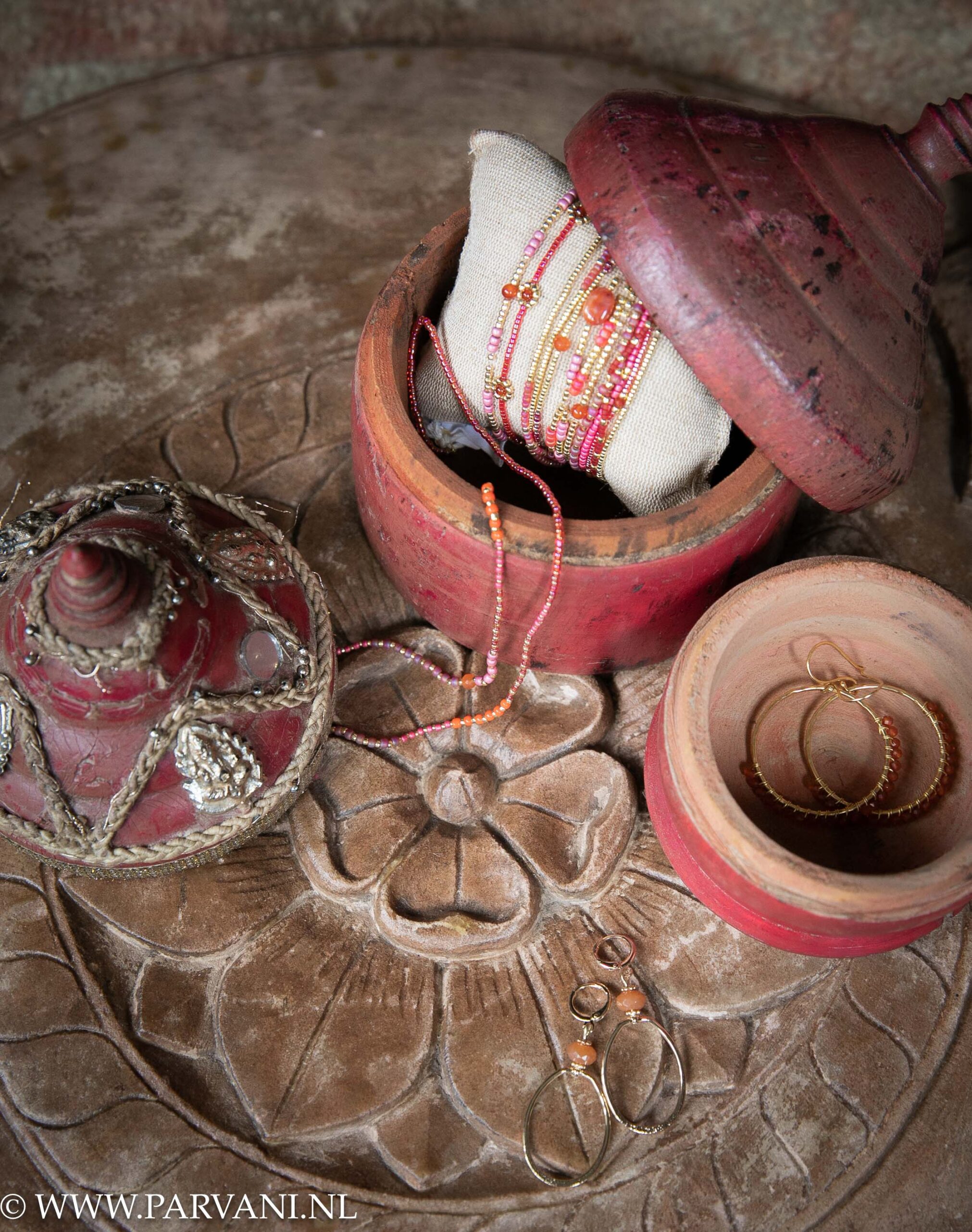 Oude rode tikapotjes op grote Indiase steen met fairtrade sieraden in warme oranje roze rode kleuren met edelsteen