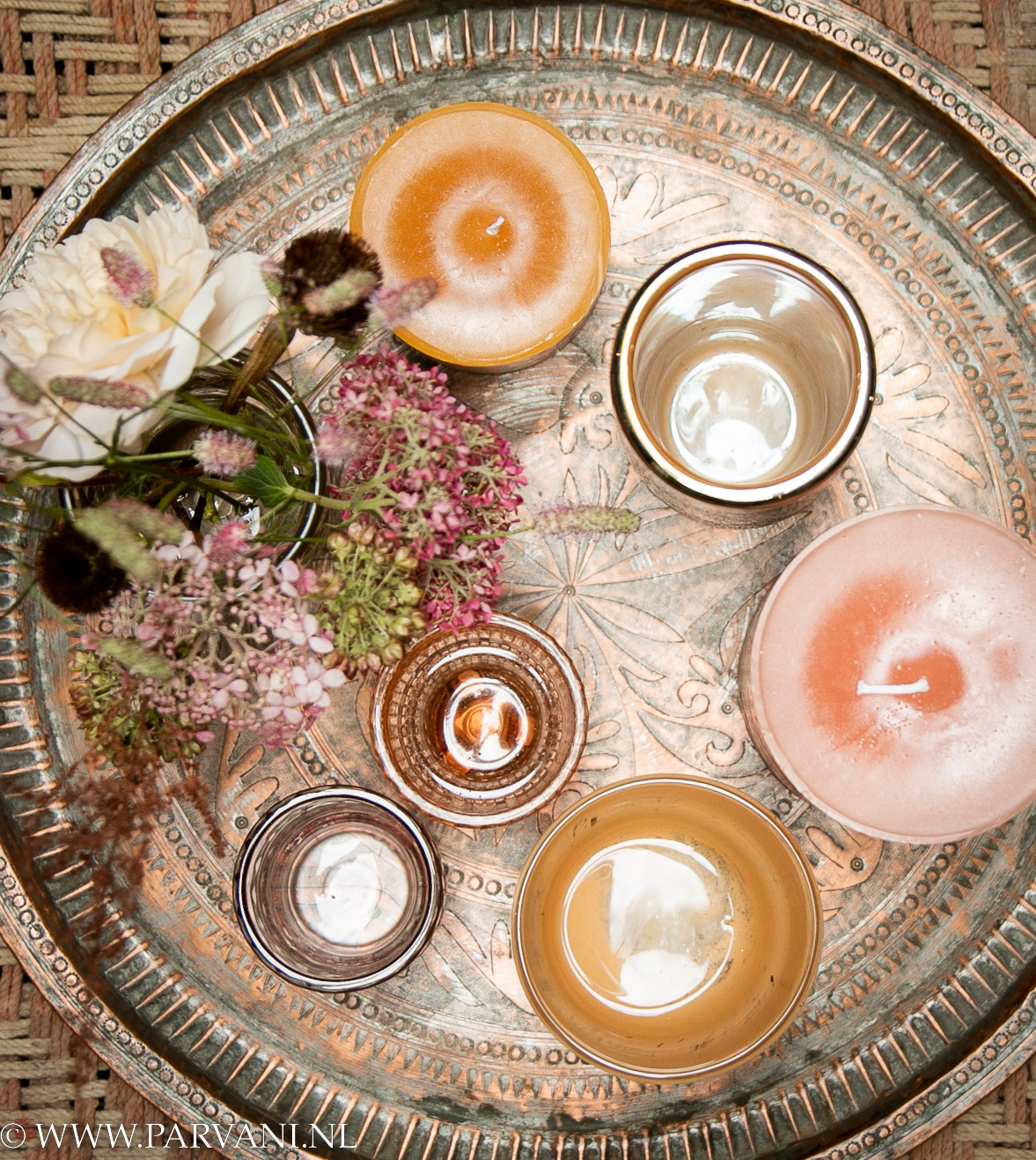 Rond koperen dienblad met gravering en roze oranje gele kleuren kaarsen, vaasjes en waxinehouders