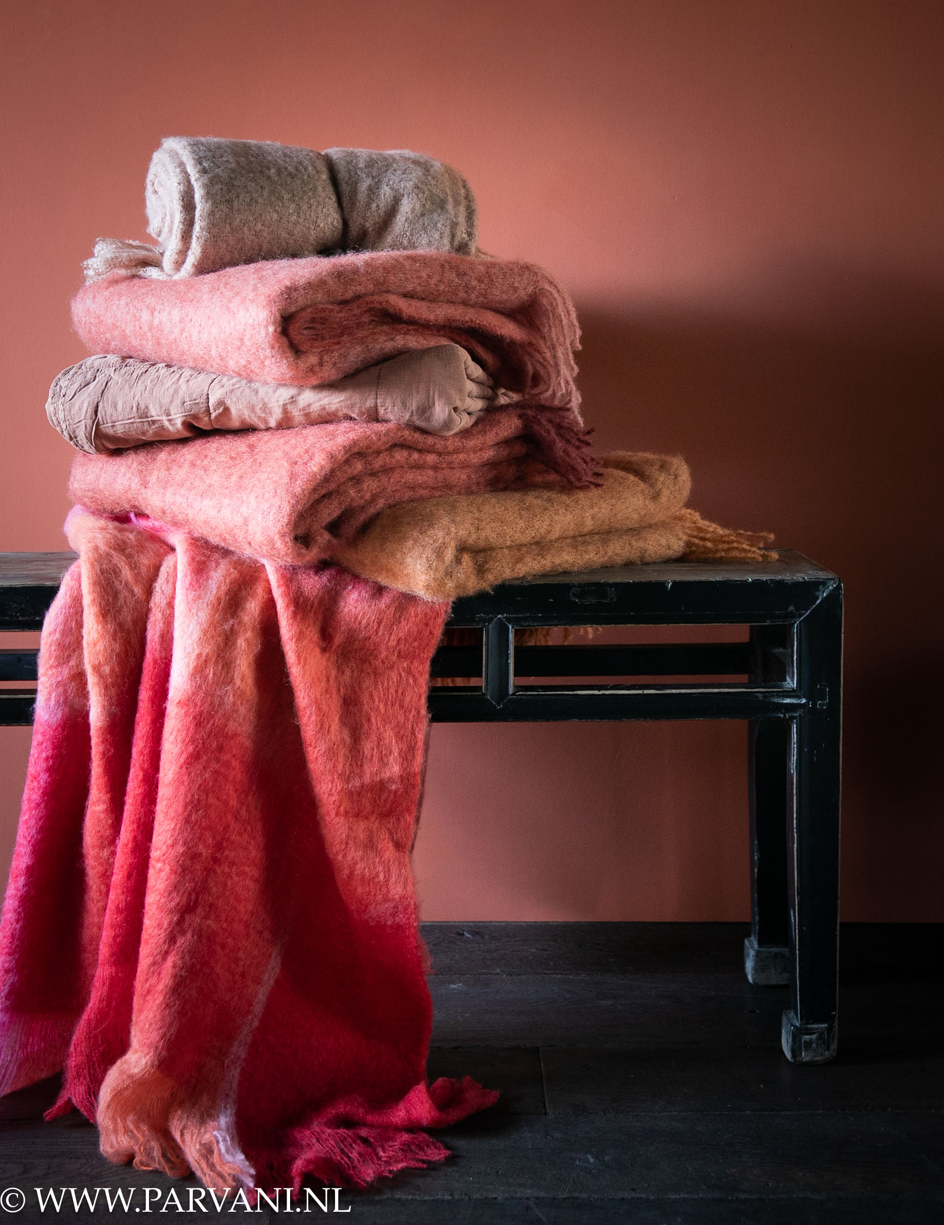 Stapel kleurrijke wollen plaids in terra, rood, oranje en roze kleuren op oud zwart houten bankje uit China