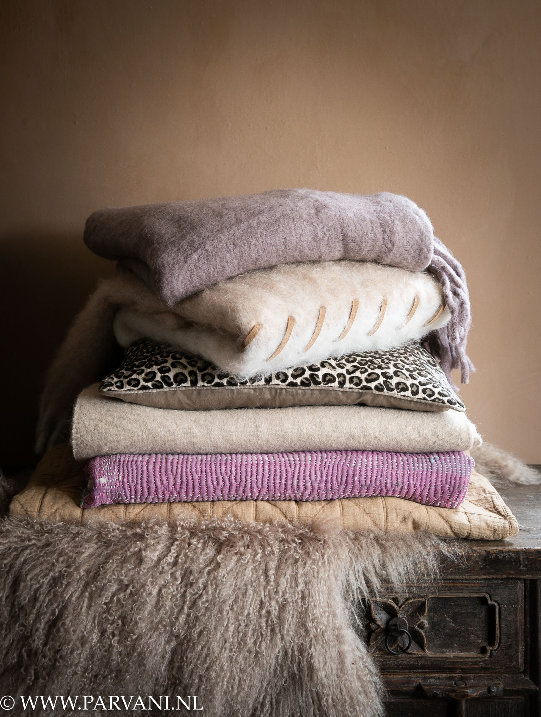 Stapel wollen plaids, mongools lamsvacht en sari deken met leopard kussen in warme nude, naturel en paars lila tinten