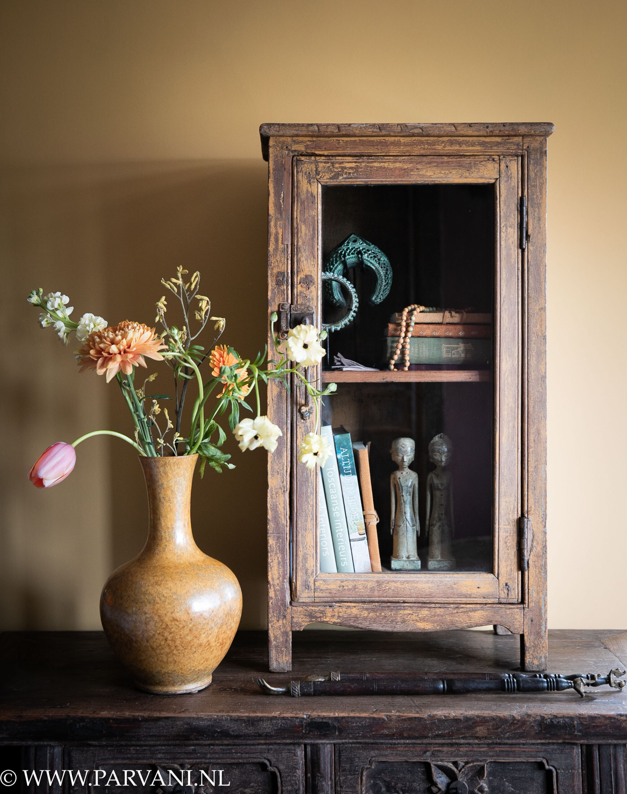 Oud houten glaskastje hangkastje uit India met okergele patina en Chinese vaas met bloemen en bronzen beeldjes en decoratie