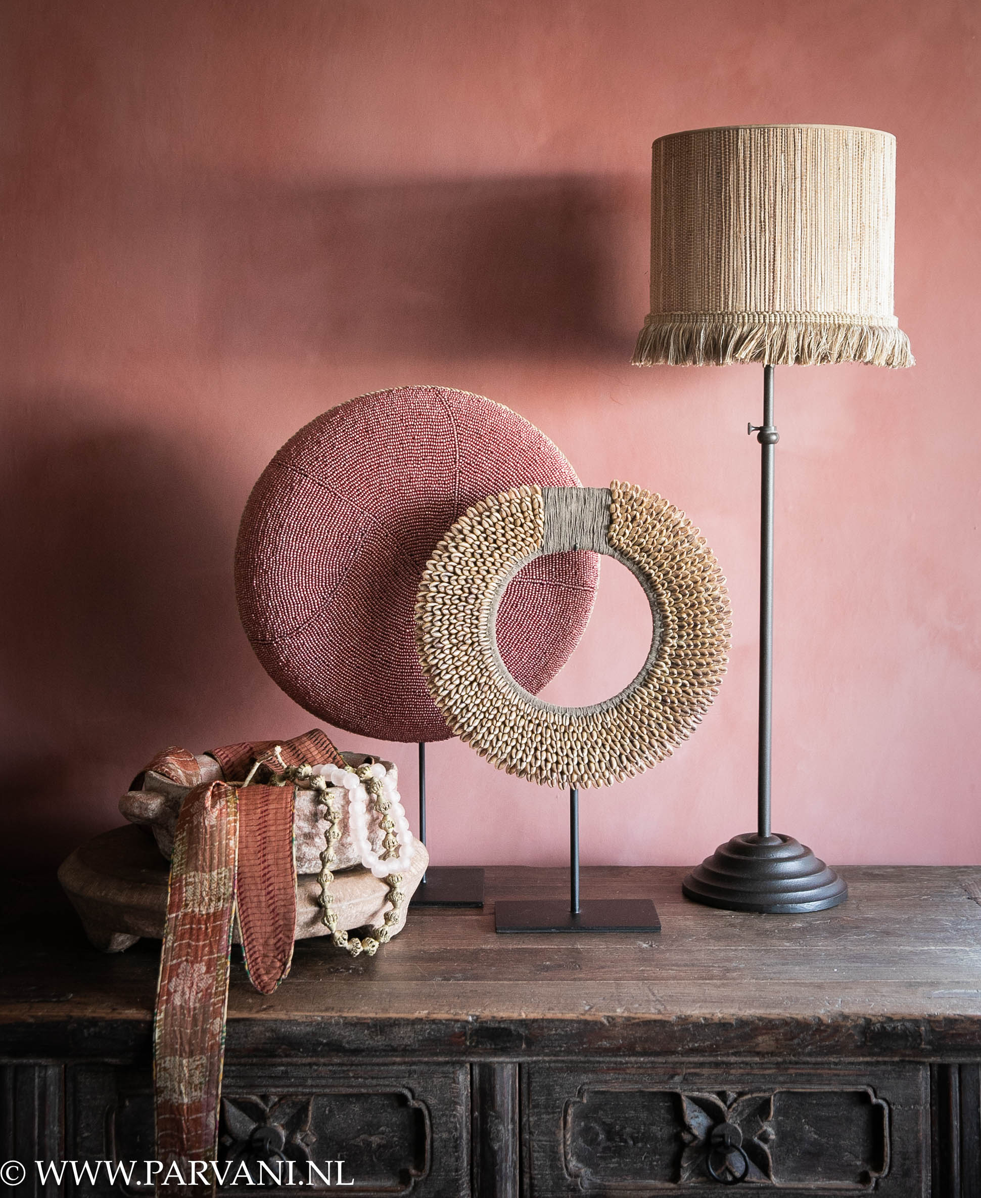 Woonaccessoires uit Indonesië met kralenschild en schelpenketting op standaard in roze en bruine kleuren, met tafellamp Delphi en bamboe lampenkapje