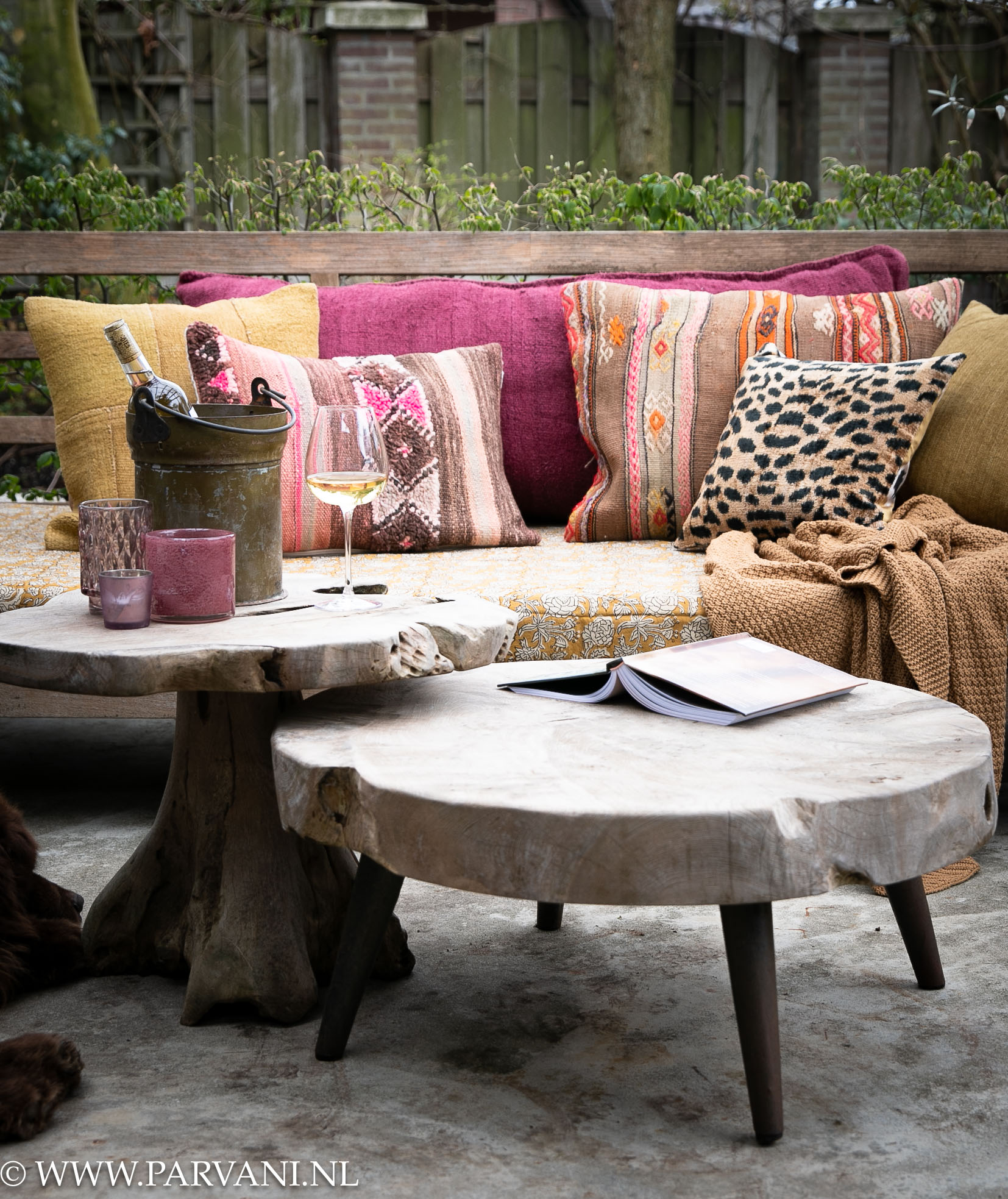 Kleurrijke kussens en batik plaid uit India op tuinbank in warme oker, geel en roze kleuren met kelim, hennep en patroon