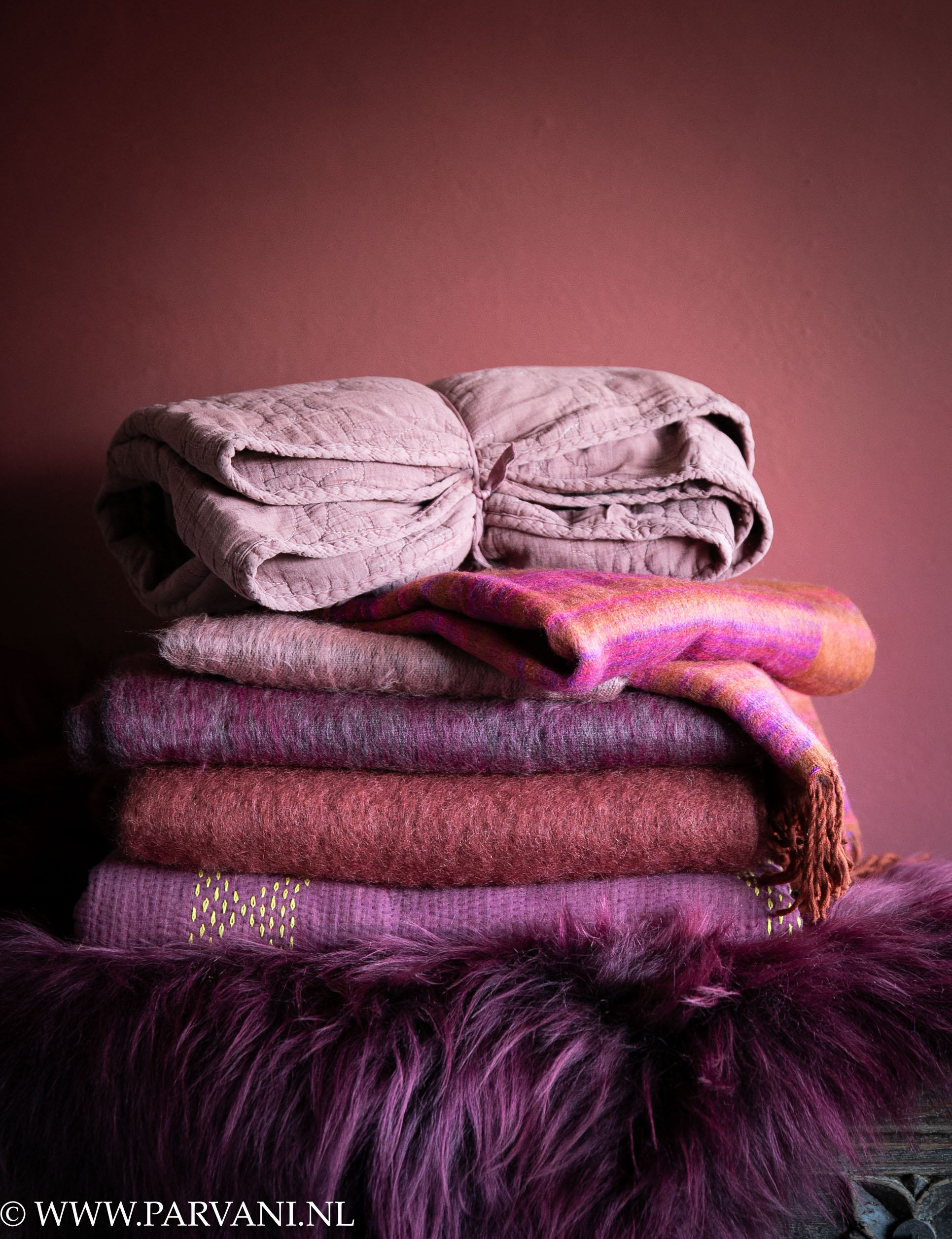 Stapel zachte plaids, sjaals en schapenvacht in warme aubergine, burgundy, paars en roze kleuren