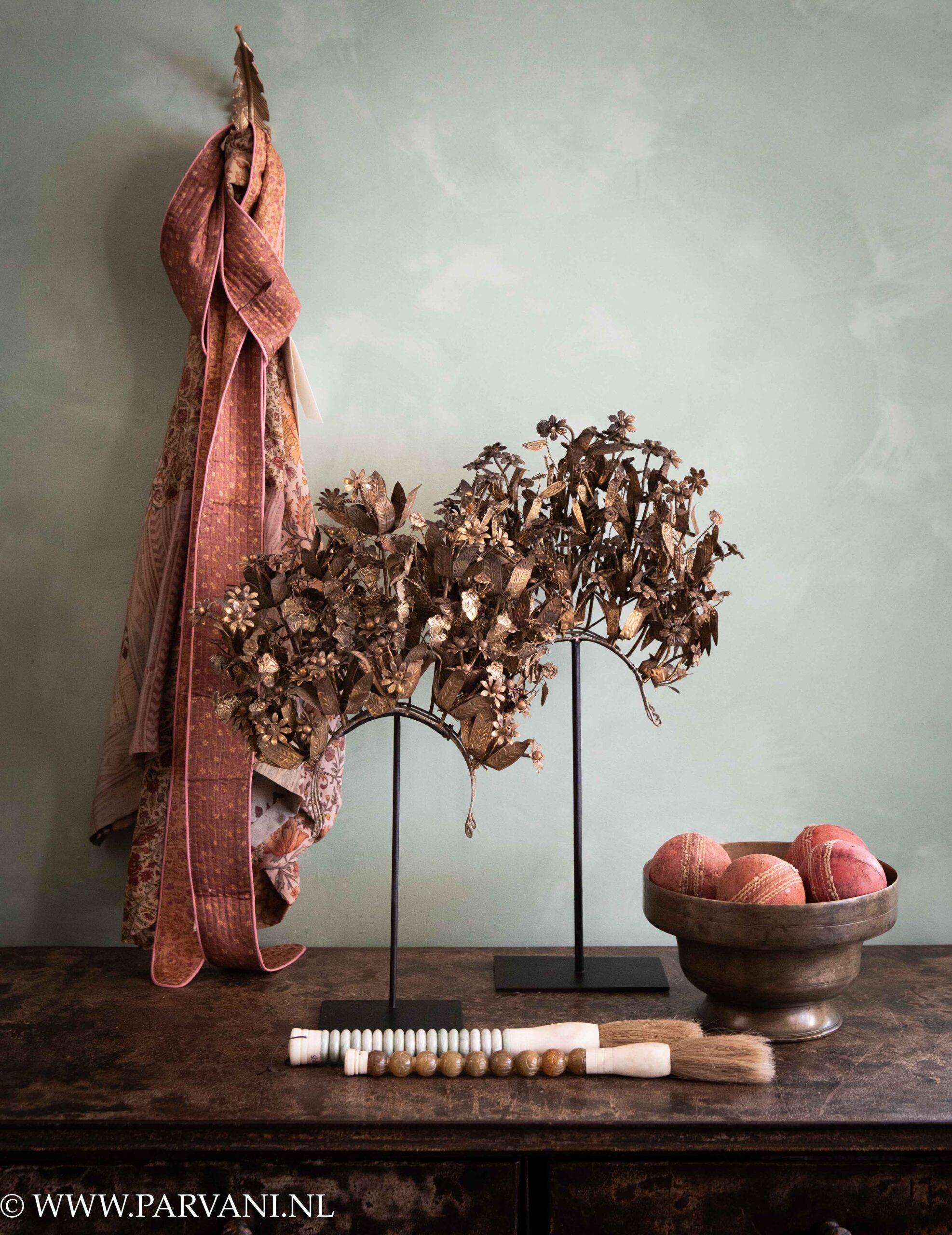 Goudkleurige Balinese kroontjes op standaard met zijde kimono van Sissel Edelbo en roze belt met bronzen schaal met cricketballen uit India